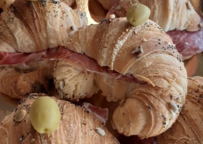 Croissant salato ripieno di prosciutto, decorato con semi e un chicco di mais, disponibili presso Dolce Pensier Pasticceria, perfetti per uno snack gustoso e raffinato.