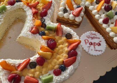 Fuga di frutta fresca e panna su torta di compleanno a forma di numero 2, decorata con fragole, kiwi, pesche, ciliegie e mirtilli, con messaggio di auguri per papà.