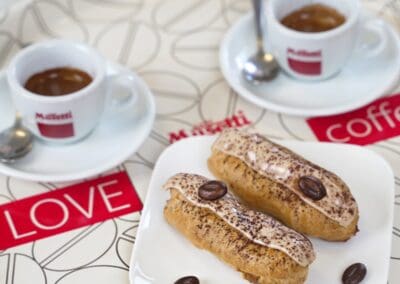 Dolce Pensier: coppia di cornetti con crema al mascarpone e decorazione di cacao, accompagnati da due tazzine di espresso, su tavolo decorato con velette love, atmosfera accogliente e dolce.