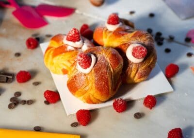Deliziosi cornetti dolci farciti, decorati con lamponi e zucchero a velo, perfetti per ogni occasione di dolce pensiero e pasticceria artigianale. Eleganza e bontà si uniscono in ogni morso.