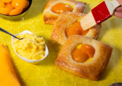 Fantasie di dolci con uova al forno e frutta, ideale per una colazione o merenda ricca di sapori e colori. Preparazione di croissant con uova e frutta, accompagnati da crema e albicocche sciroppate.