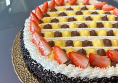 Fiore di crema e frutta sulla torta con decorazioni di fragole e cioccolato, perfetta per occasioni speciali, presentata su un piatto dorato elegante.