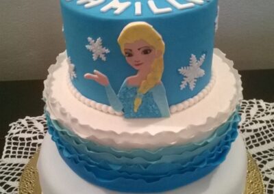 Torta di compleanno a tema Frozen con decorazioni di Elsa, Olaf e fiocchi di neve in pasta di zucchero, su base bianca e blu, perfetta per festeggiare un compleanno speciale.