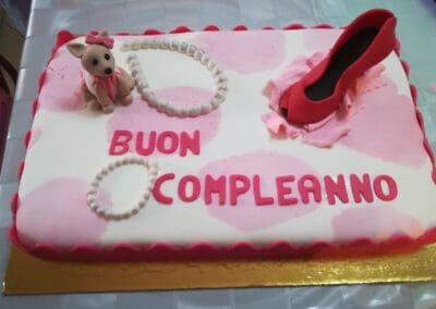 Cerimonia di compleanno con torta decorata con scarpa rossa e pupazzo dog con fiocco rosa, ideale per celebrare un traguardo speciale con dolcezza e stile.