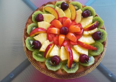 Frutta fresca e colorata su crostata dolce, con fette di kiwi, ananas, fragole, ciliegie e pesche, presentata su un piatto decorativo dorato, ideale come dessert estivo.