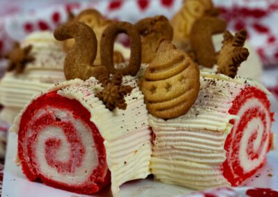 Delizia di pasta biscotto rossa ripiena di crema, decorata con biscotti natalizi e numeri in pasta, perfetta per festeggiare il Natale con un dolce speciale.